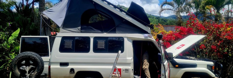 Auto mit geöffneten Dachzelt und Hube. Mann zieht ein neues Kabel von den Solarpanels zur Batterie.