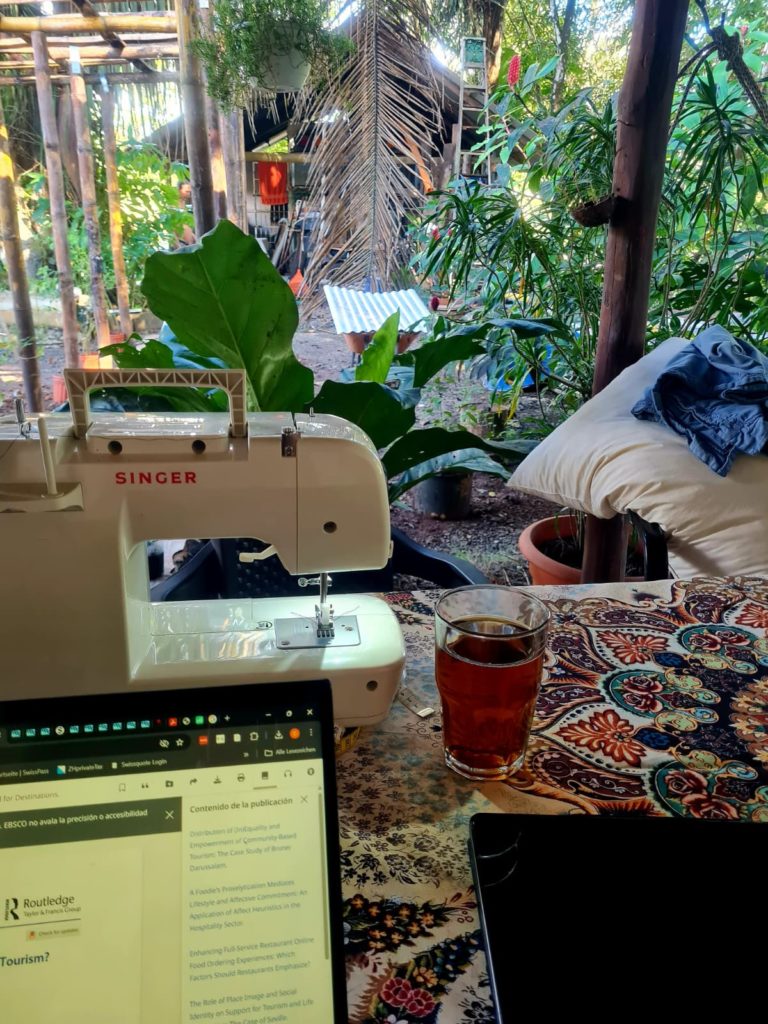 Tisch vollgestellt mit Nähmaschine, Laptop und ein Glas Tee